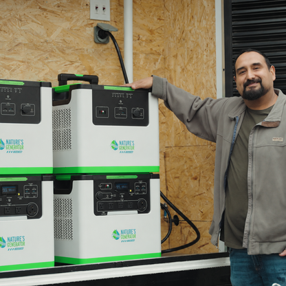 A man in a gray jacket stands next to a stack of white and green portable power stations branded Nature's Generation, set against an OSB wood wall background.