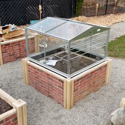 Brick-built raised garden bed with a glass roof in an outdoor setting.