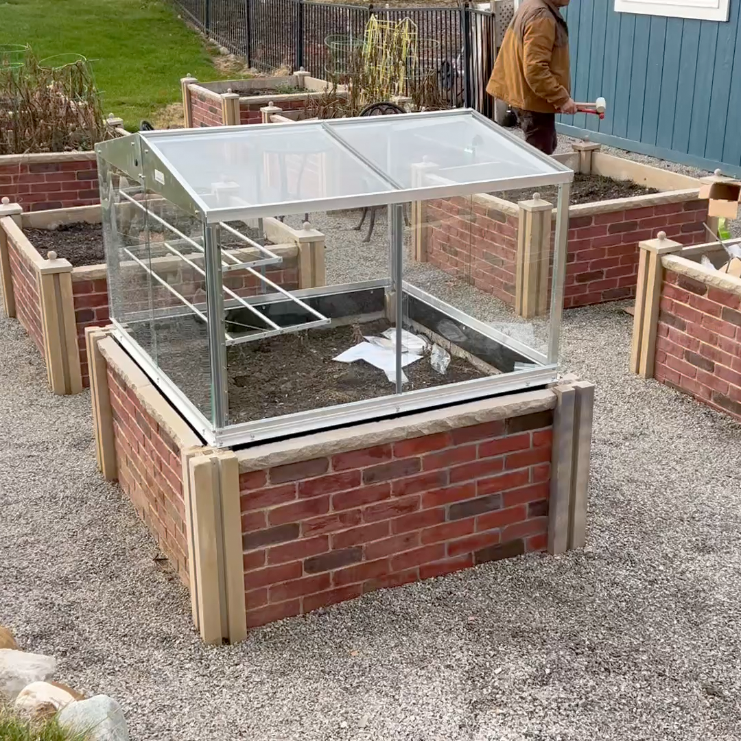 Brick-built raised garden bed with a glass cover in an outdoor setting.
