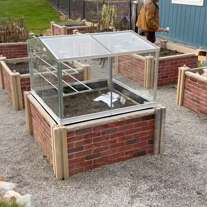 Brick-built raised garden bed with a glass cover in an outdoor setting.