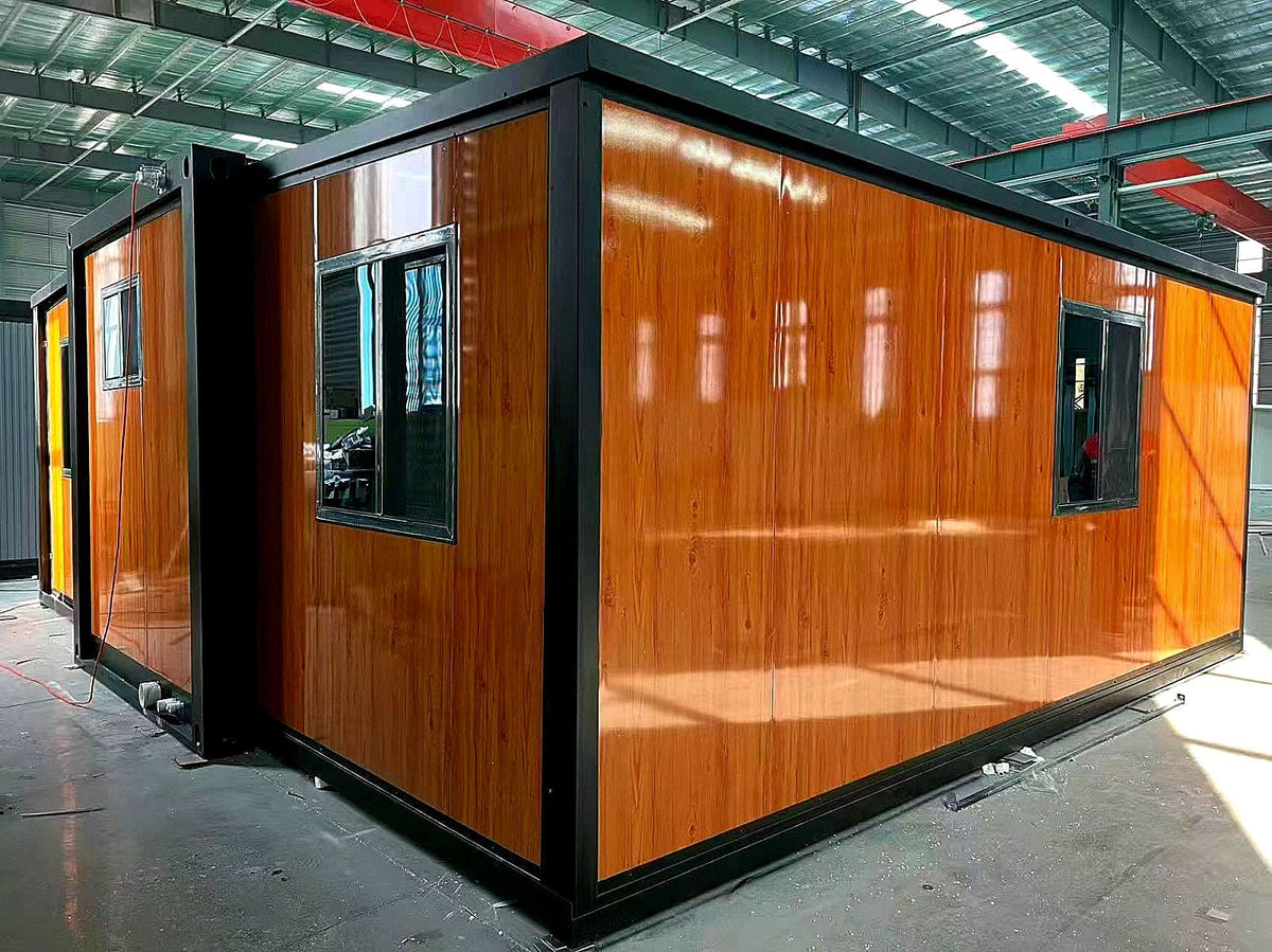 A modular home with a glossy orange-brown wood grain finish and black metal framing, shown inside a warehouse.