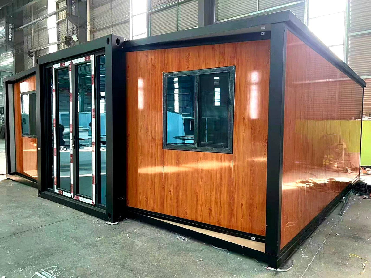 A modular home with a warm wood-grain exterior paneling and a black metal frame, shown in an industrial warehouse setting.